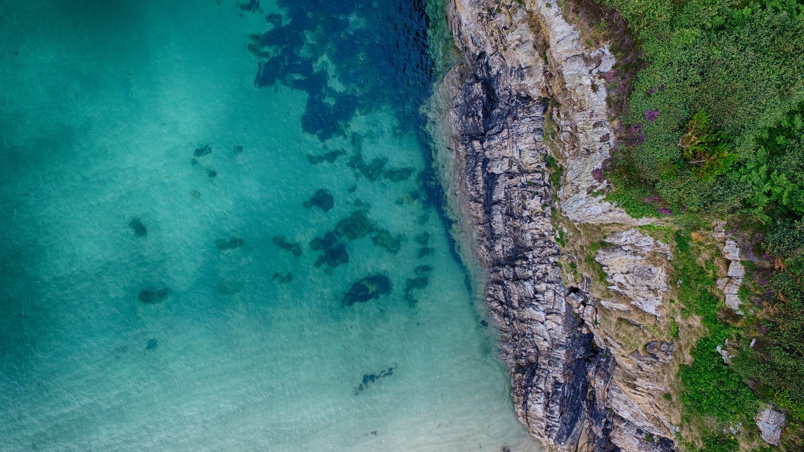 Straight down at a grey cliff edge and clear turquoise water, 4:06 pm, July 10.