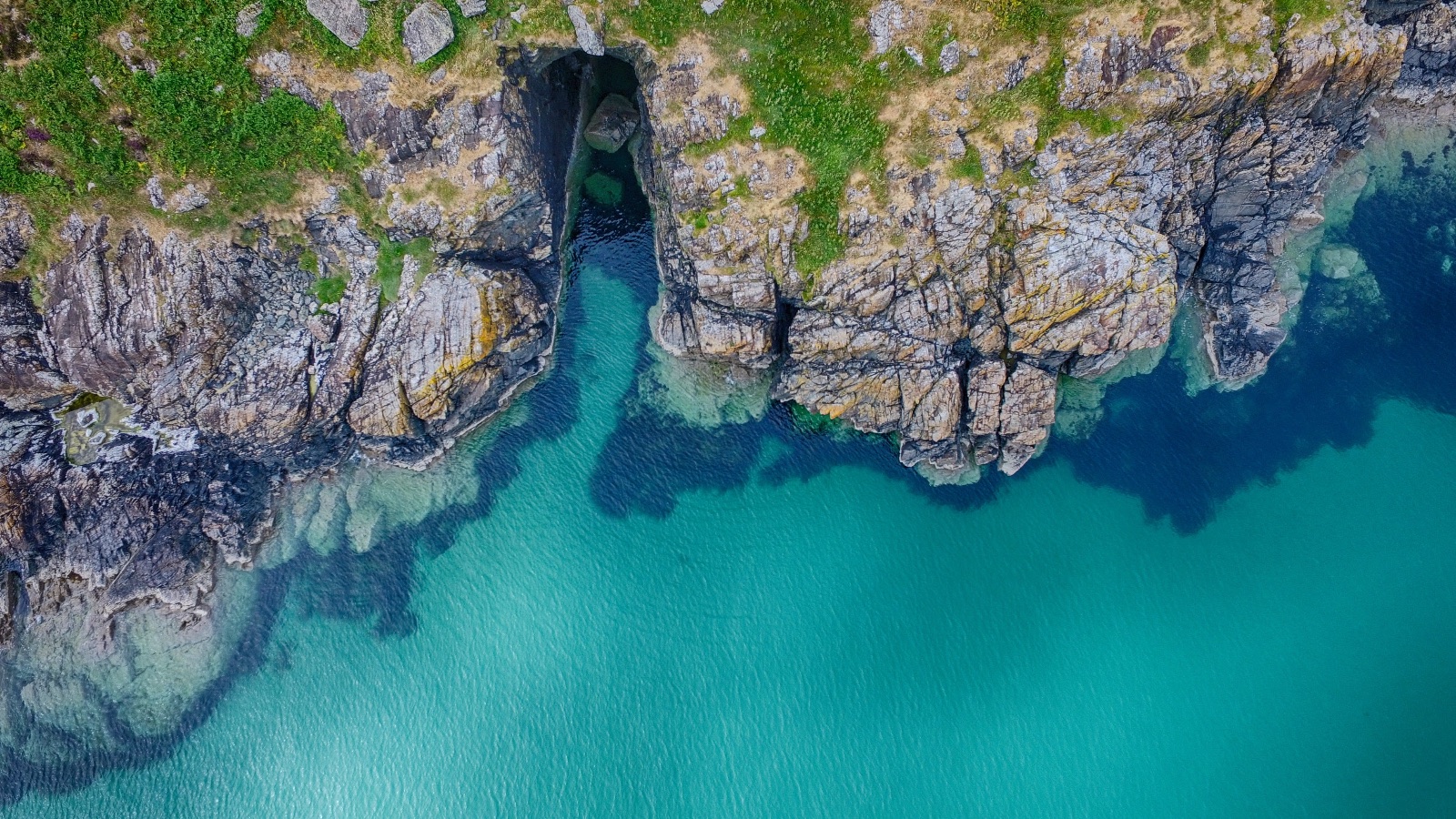 A narrow cave cut back into the rock, green water running into it.