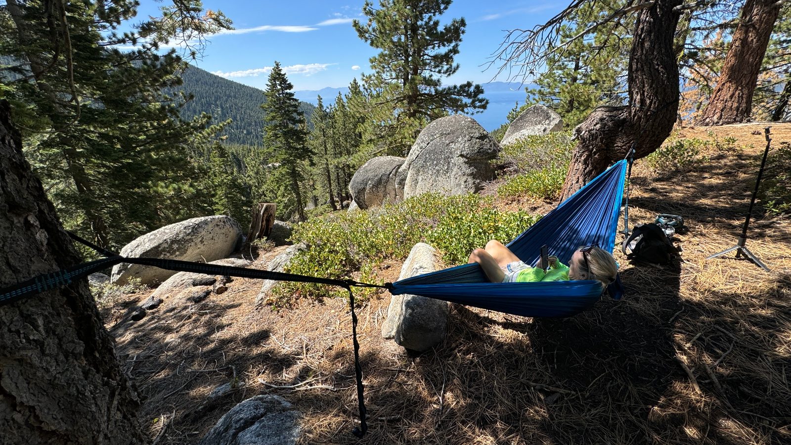 11:25. A blue hammock between two pines, granite boulders and the lake through the trees.