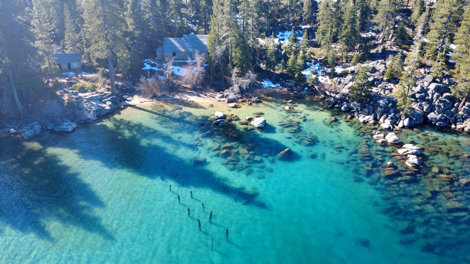 10:16. A small cove, old buildings in the trees and a line of old posts in the water.