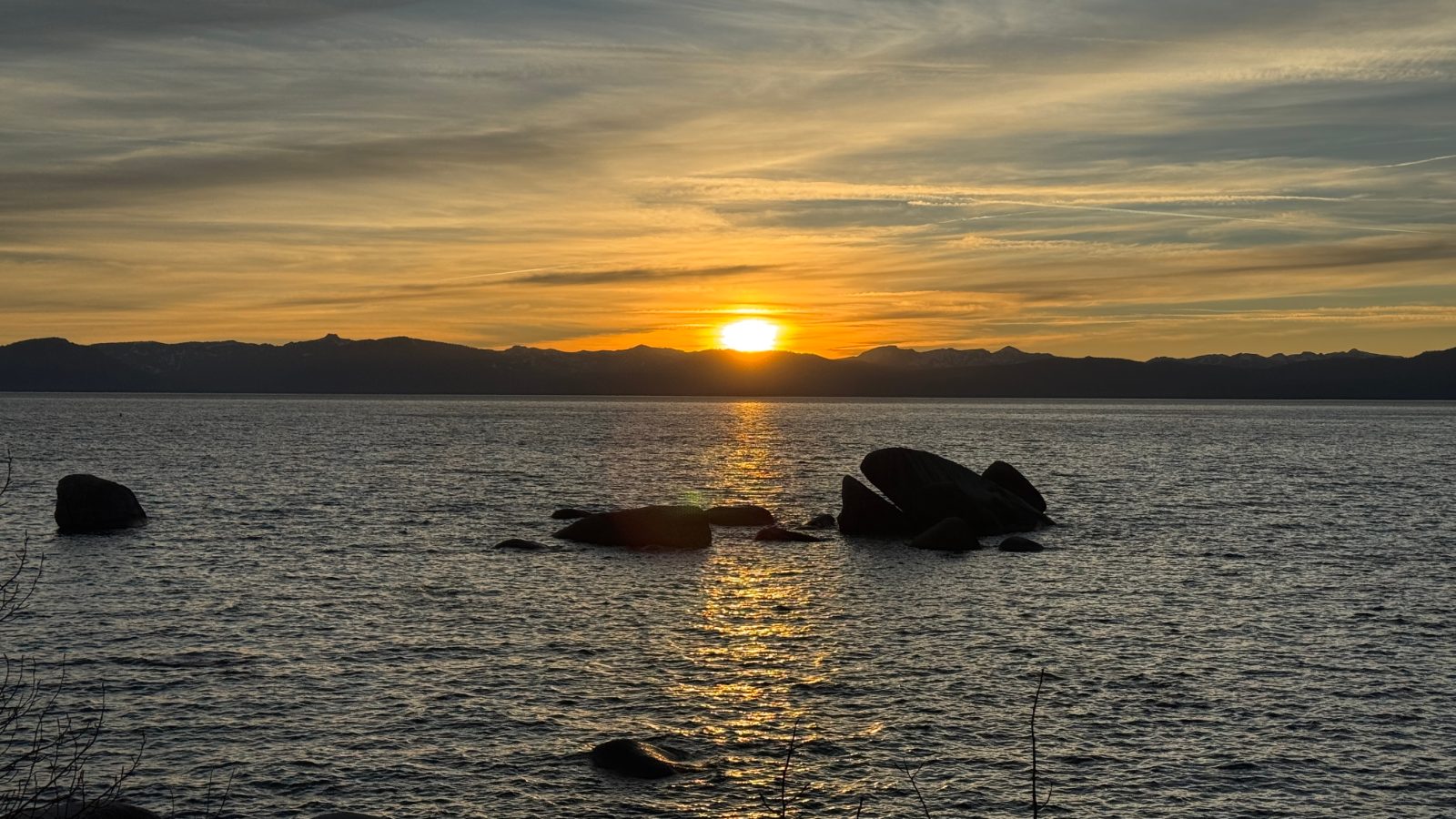 7:09 PM: the sun going down behind the mountains across the lake, the whale rocks in silhouette.