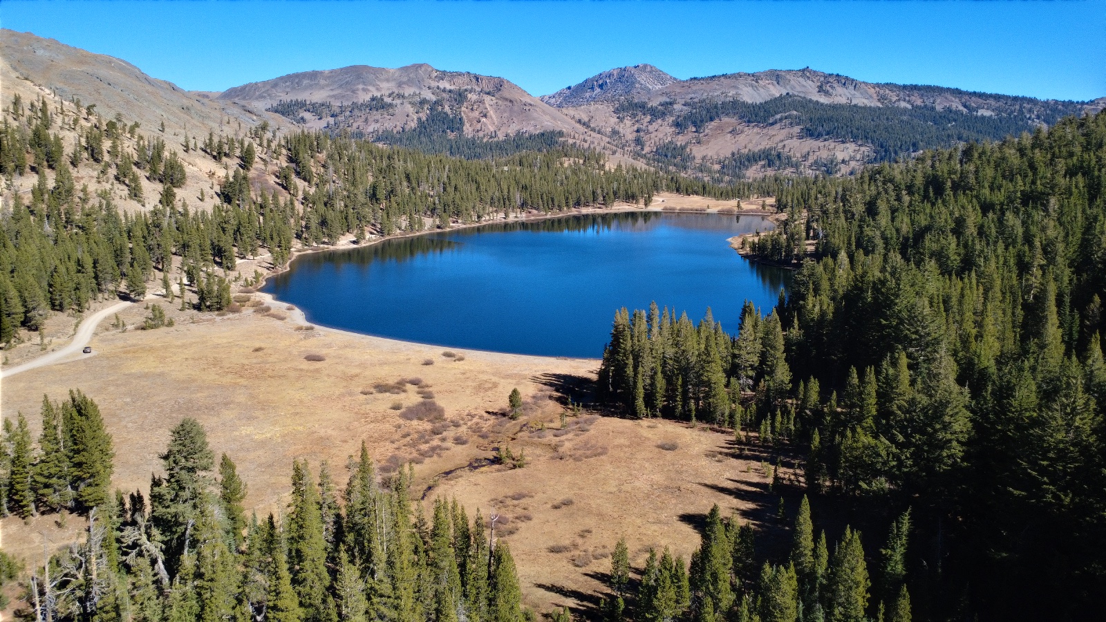 A blue lake past a dry meadow, peaks behind it.